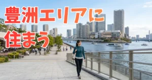 晴天の豊洲のウォーターフロントを歩く、黒髪ポニーテールで青緑色のニットと黒いパンツ姿の女性。水辺の遊歩道を笑顔で歩いており、背景には穏やかな運河と行き交う遊覧船、タワーマンション群や大型商業施設が広がっている。